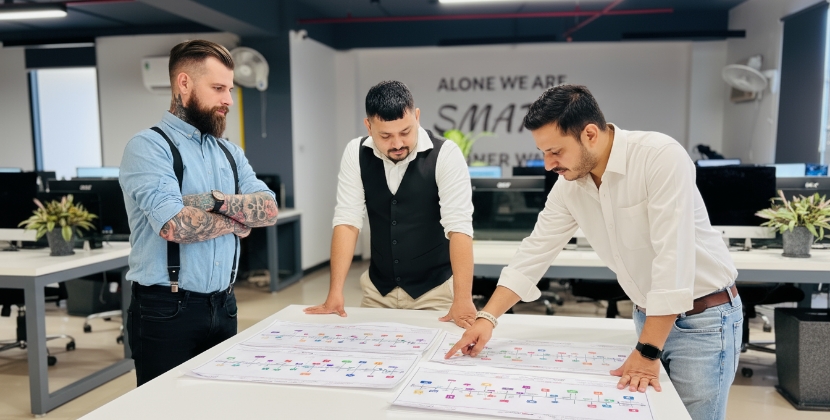 Drie mannen bekijken webshop architectuur en flowcharts op tafel in kantoor