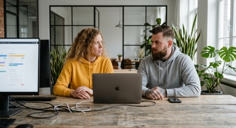Twee collega's kijken elkaar aan bij bureau, gesprek over vaktaal en buzzwords