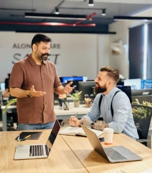 Two colleagues discussing a project at a desk with laptops
