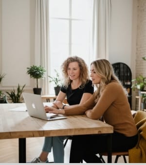 Two colleagues collaborating at a laptop in a bright workspace