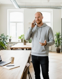 Collega voert een telefoongesprek in een open kantoor, met laptop en notitieboek op tafel.