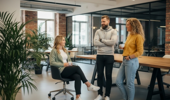 Studio Ubique teamoverleg in open kantoor, drie collega’s bij grote tafel met planten