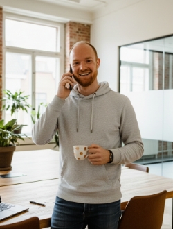 Studio Ubique collega aan de telefoon met koffiemok, informele remote-first werkdag