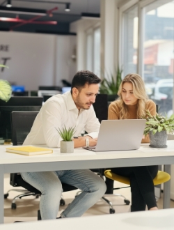 Samen werken aan laptop in open kantoor, Studio Ubique teammoment met koffiebeker
