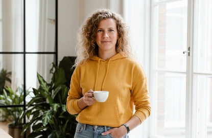 Portret van Sanne, teamlid van Studio Ubique, met koffiekopje in een lichte kantooromgeving