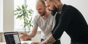 Twee collega’s bespreken UX en UI ontwerp bij een webdesign bureau aan een bureau met groot scherm en laptop.
