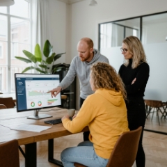 Drie collega's bespreken progressive web app laten ontwikkelen aan de hand van een PWA-dashboard op groot scherm