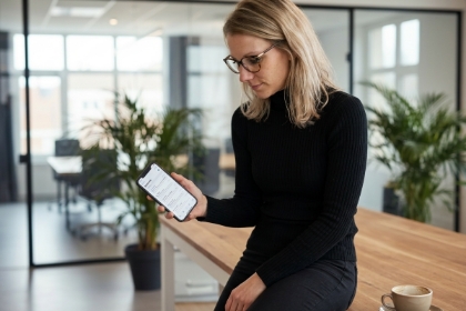 Vrouw bekijkt native iOS app laten ontwikkelen in Swift op iPhone, zittend in licht kantoor met planten