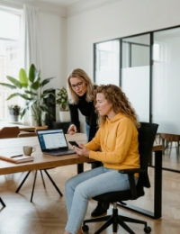 Twee collega's bespreken PWA ontwikkelen: staande vrouw wijst naar laptop terwijl andere collega smartphone vasthoudt
