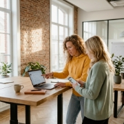 Twee collega's vergelijken installeerbare web app op laptop en smartphone in modern kantoor met bakstenen muur