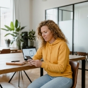 Vrouw vergelijkt iPhone app ontwikkelen op smartphone en laptop aan kantoortafel met daglicht