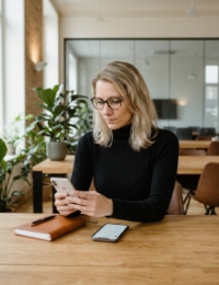 Vrouw met bril controleert een iOS app laten ontwikkelen op haar smartphone aan een houten kantoortafel