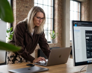 Front-end developer working on laptop and monitor in industrial loft office with brick walls