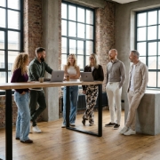 Zes Studio Ubique collega's rond een hoge houten tafel in het Zwolse industriële kantoor, volledige teamcompositie