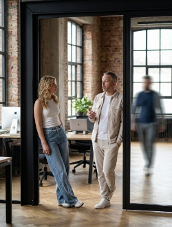 Two colleagues in conversation in the doorway of a meeting room in the Zwolle industrial office, colleague walking past with motion blur