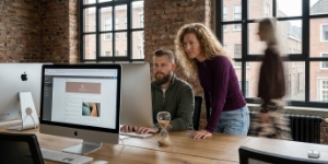 Teamleden bekijken CMS-publicatiescherm op iMac terwijl collega voorbijloopt