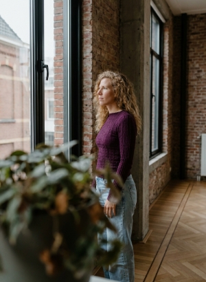 Colleague looking out of a tall industrial window in side profile, soft daylight on her face