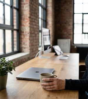 Hand met een keramische koffiemok op een houten bureau in een Zwols industrieel kantoor, zacht daglicht