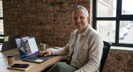 Developer at a wood desk in a Zwolle office reviewing a plain-text llms.txt file on screen next to an AI search results panel