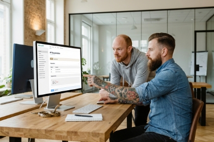 Twee teamleden bij een admin-scherm op een iMac, Node.js en NestJS
