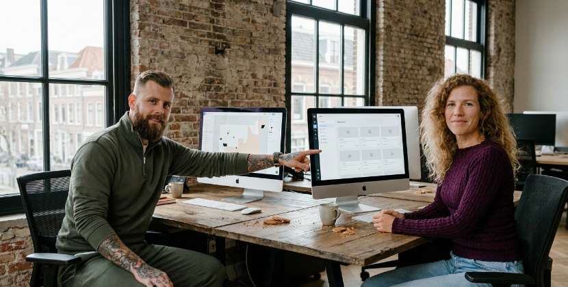 Two designers in a Zwolle office reviewing two monitors with different CMS interfaces side by side