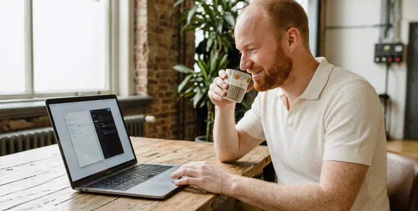 Persoon vergelijkt twee schermpanelen op laptop met koffiekopje in hand