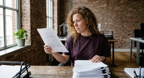 Marketeer houdt een geprint zoekwoordvel tegen het raamlicht naast een stapel papier
