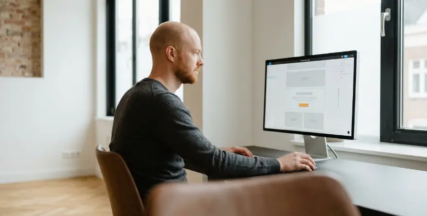 Persoon vergelijkt een sollicitatieformulier op een telefoon met hetzelfde formulier op een desktopscherm in een Zwols kantoor