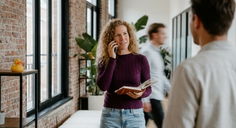 Marketeer loopt bellend door een studiokantoor met een notitieboek, midden in een B2B SEO gesprek