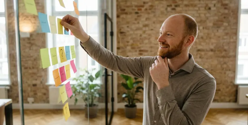 Marketer at a glass wall of sticky notes, mapping a B2B SEO funnel by buyer intent in a studio office
