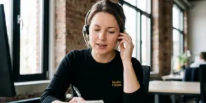 Bella, Studio Ubique's AI receptionist, answering a phone call on a headset while taking a note