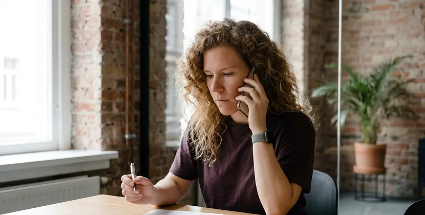 Person on a phone call in a glass meeting room, looking down at a printed proposal