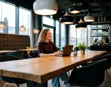 Collega werkt op een laptop aan de lange houten tafel in het kantoor van Studio Ubique in Zwolle