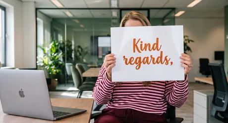 Vrouw houdt een kaart met Kind regards in oranje glittersierschrift voor haar gezicht