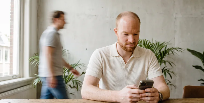 Persoon leest aan een kantoorbureau een mail op de telefoon, één wenkbrauw opgetrokken