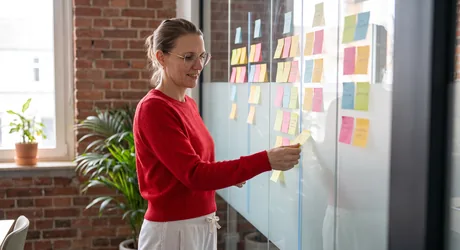 Person moving a sticky note between columns on a glass wall while sorting out product field ownership