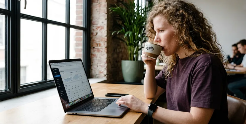 Persoon bekijkt rustig een productdata-synchronisatie op een MacBook tijdens de maandelijkse controle, koffie binnen handbereik