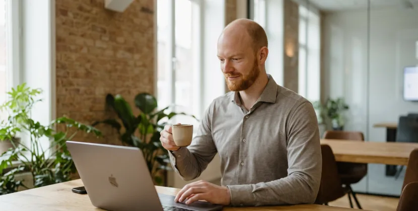 Sitebeheerder met koffie controleert een beheerpaneel op een laptop tijdens de maandelijkse check