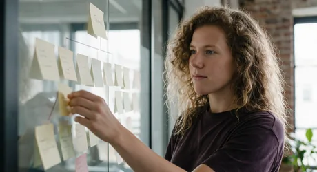 Marketeer verplaatst een sticky note hoger in een paginastructuur op een glazen wand